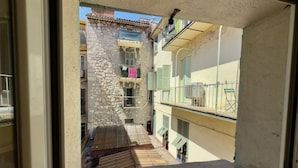 Une vue depuis une fenêtre d’un immeuble à la façade en pierre, doté de balcons avec des garde-corps et d’un petit espace extérieur avec une terrasse en bois.