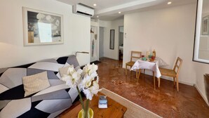 Un salon moderne avec un canapé, une table à manger et des chaises, un vase de fleurs et un tableau encadré au mur.
