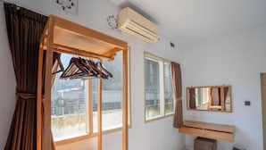 Une pièce avec un bureau en bois, un miroir, un portant à vêtements et une fenêtre avec des rideaux.