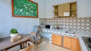 Une cuisine équipée d’une table à manger, de chaises, d’un réfrigérateur, d’un four à micro-ondes et d’un évier. Il y a une étagère au-dessus du plan de travail et un tableau décoratif au mur.