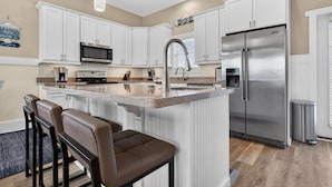 A modern kitchen with white cabinetry, stainless steel appliances, a granite countertop, and a bar area with stools. - Isle Always Luv View-New To Rental Market, 5beds/Pet Friendly/Ocean Views (ocean isle beach)