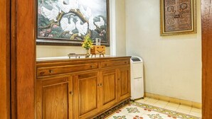 A wooden cabinet with a window above it, a framed artwork of doves, and a patterned floor. - Ndalem Kartowikoro 1835 (Surakarta)