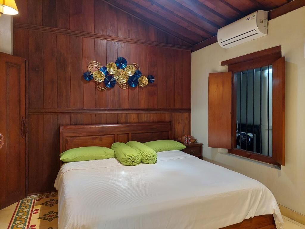A neatly made bed with green pillows, a wooden headboard, and a decorative wall piece.