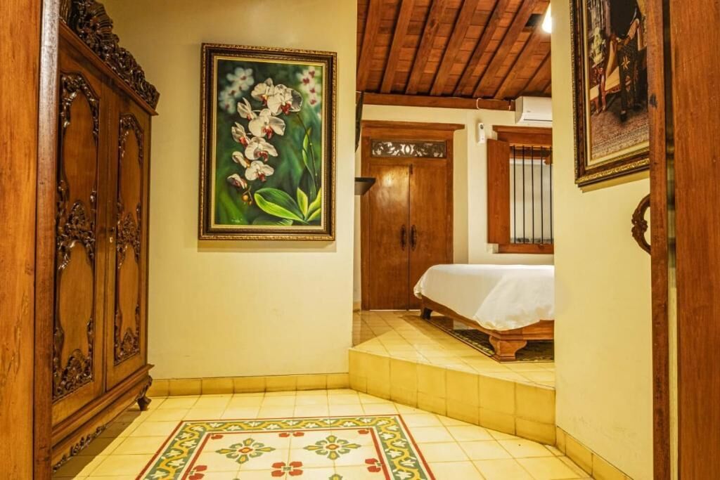 A hotel room with a bed, wooden wardrobe, and a painting of flowers on the wall.