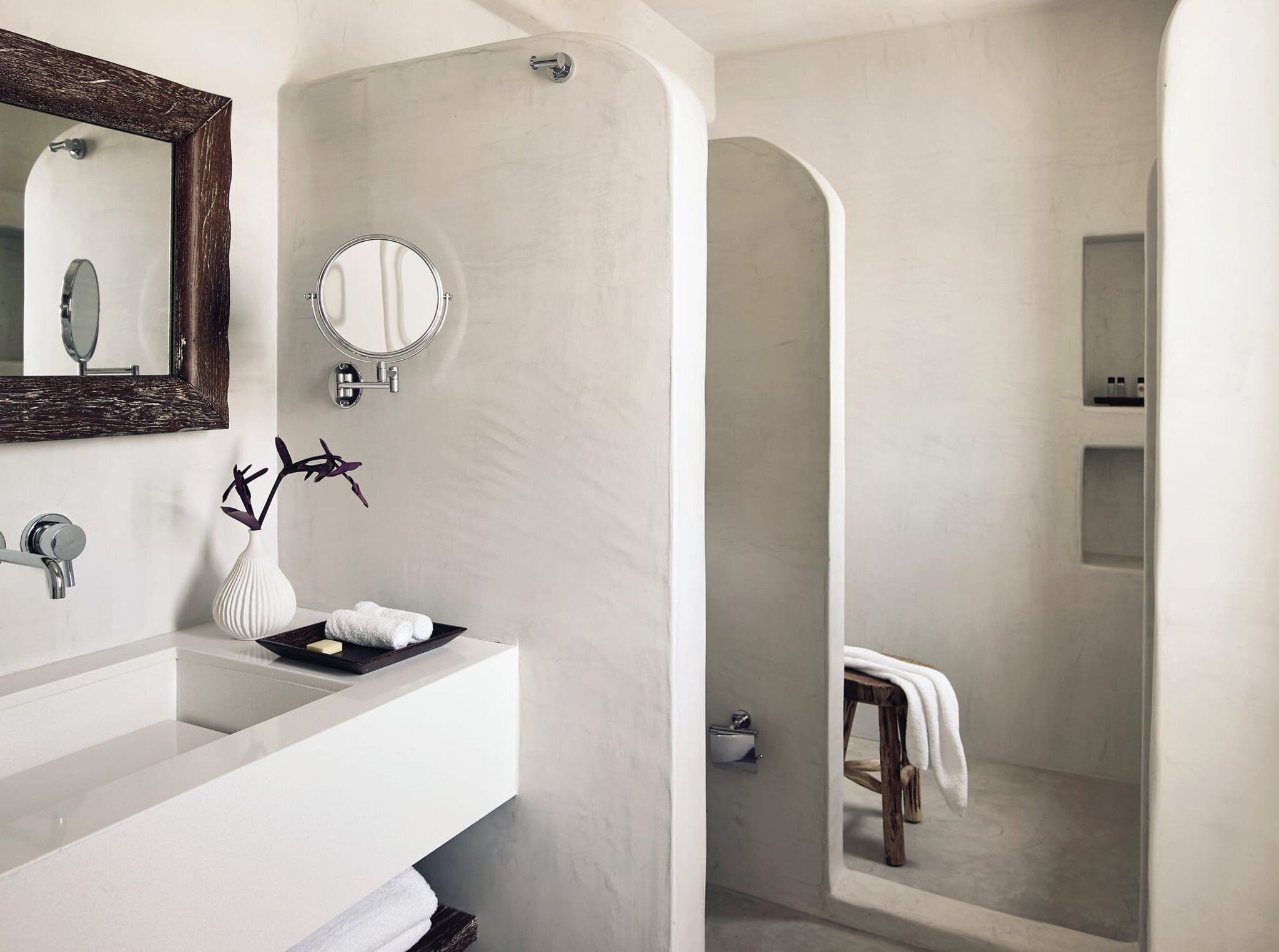 A modern bathroom with a white vanity, a large mirror, a round mirror, and a shower area with a wooden stool.
