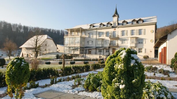A large, multi-story building with a prominent tower, surrounded by snow-covered gardens and trees.