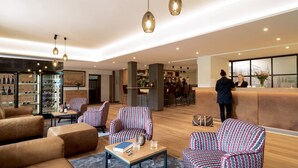 A modern hotel lobby with leather sofas, patterned armchairs, a reception desk, and a bar area.