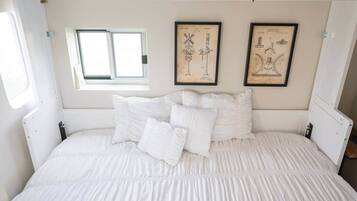 A bed with white bedding and pillows, a small window, and two framed vintage technical drawings on the wall.