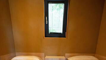 A small, single room with two beds, a window, and a wooden cabinet.