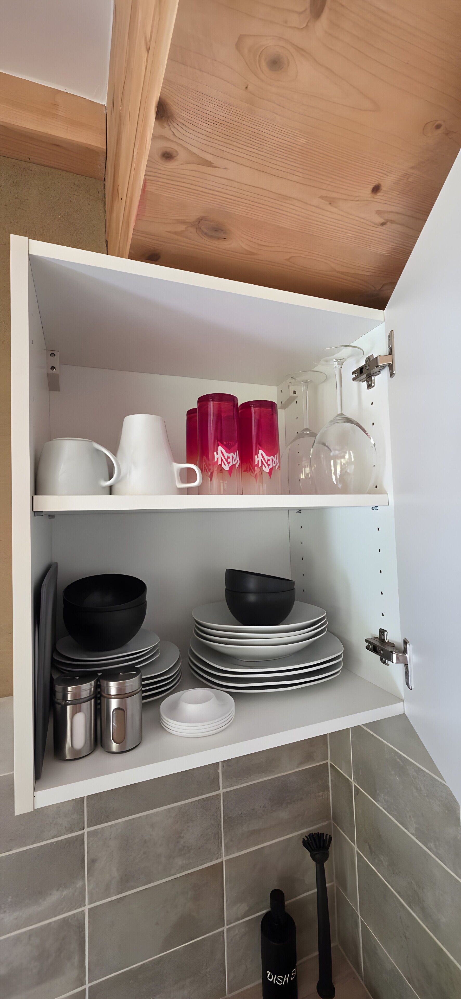 Un armario de cocina con vajilla, tazas y una botella, todo en blanco y negro.