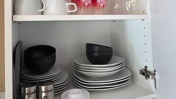 Un armario de cocina con vajilla, tazas y una botella, todo en blanco y negro.