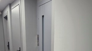 Ein Korridor mit grauen Wänden und Türen, einem Teppichboden und einer Deckenleuchte.