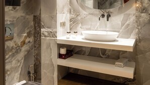 Ein modernes Badezimmer mit Marmorwand, einem runden Spiegel, einem weißen Waschbecken und einer Toilette.