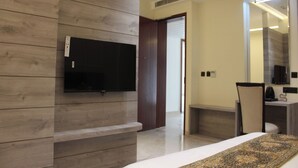 Une chambre d’hôtel moderne dotée d’un téléviseur à écran plat fixé sur un mur en panneaux de bois, d’une cheminée, d’un coin repas avec une table et des chaises, et d’un grand miroir au-dessus du meuble-miroir.