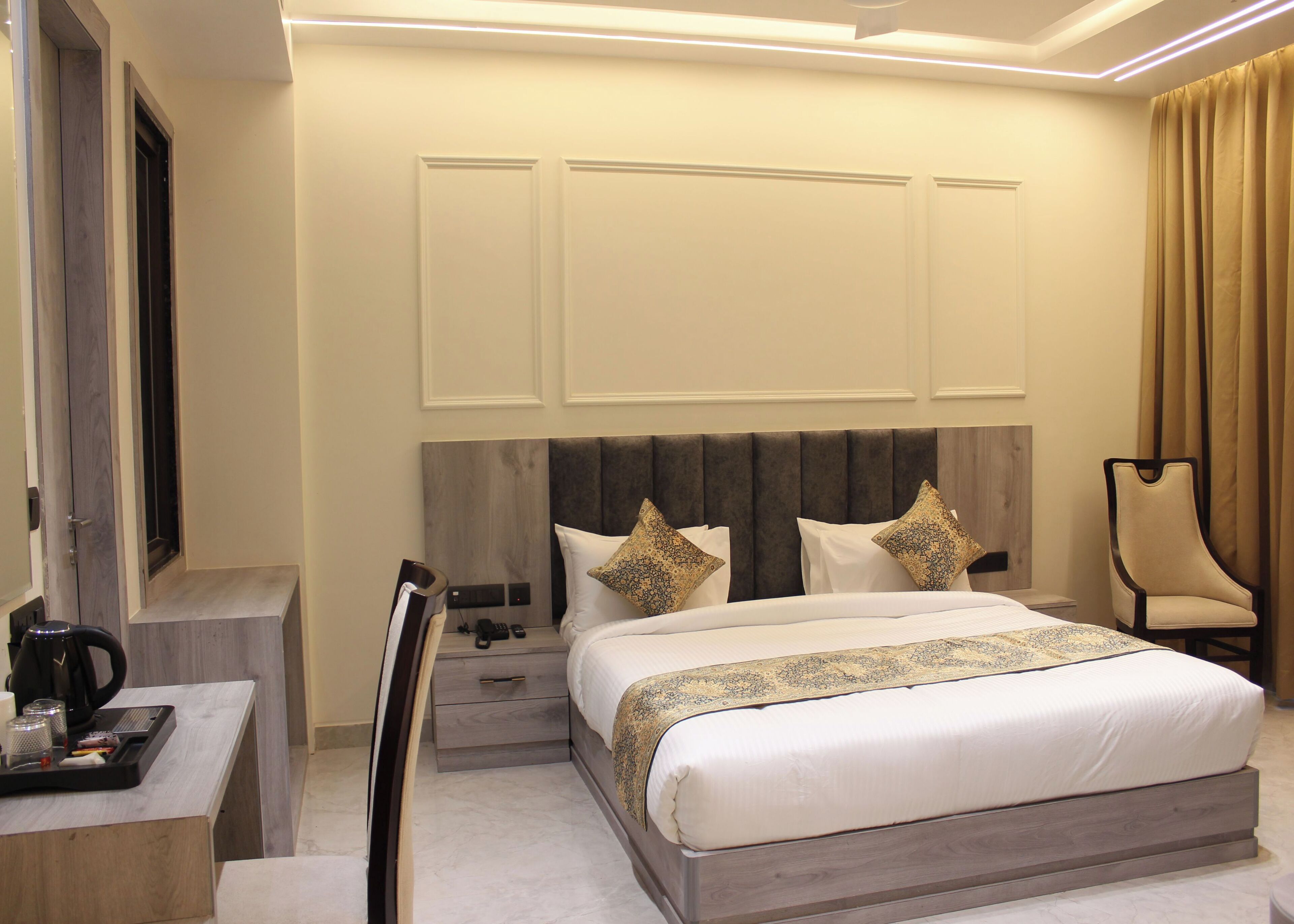 A hotel room with a large bed, bedside tables, a desk with a chair, and a chair by the window.