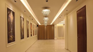 Un couloir orné d’un lustre, avec des œuvres d’art encadrées accrochées aux murs, et une porte en bois au bout.
