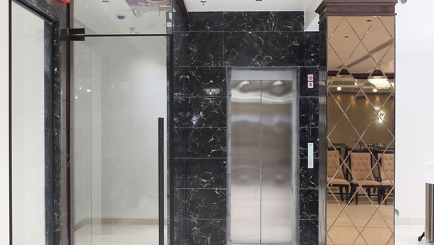Un ascenseur moderne doté d’une porte en verre, de murs en marbre et d’un espace détente avec des fauteuils.