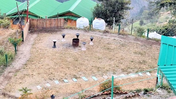 A rural setting with green-roofed buildings, a dirt path, and a mountainous backdrop. - Anany Resort (Pangoot)