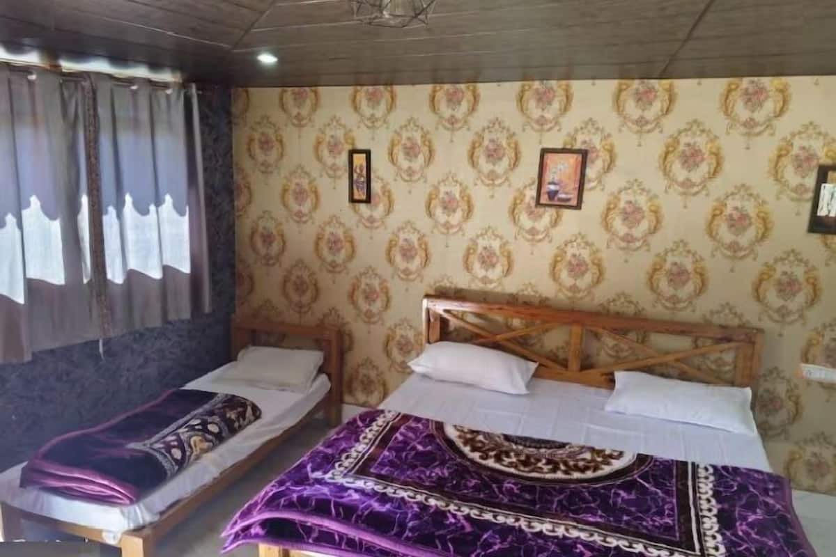 A room with two beds, patterned wallpaper, and a wooden headboard.