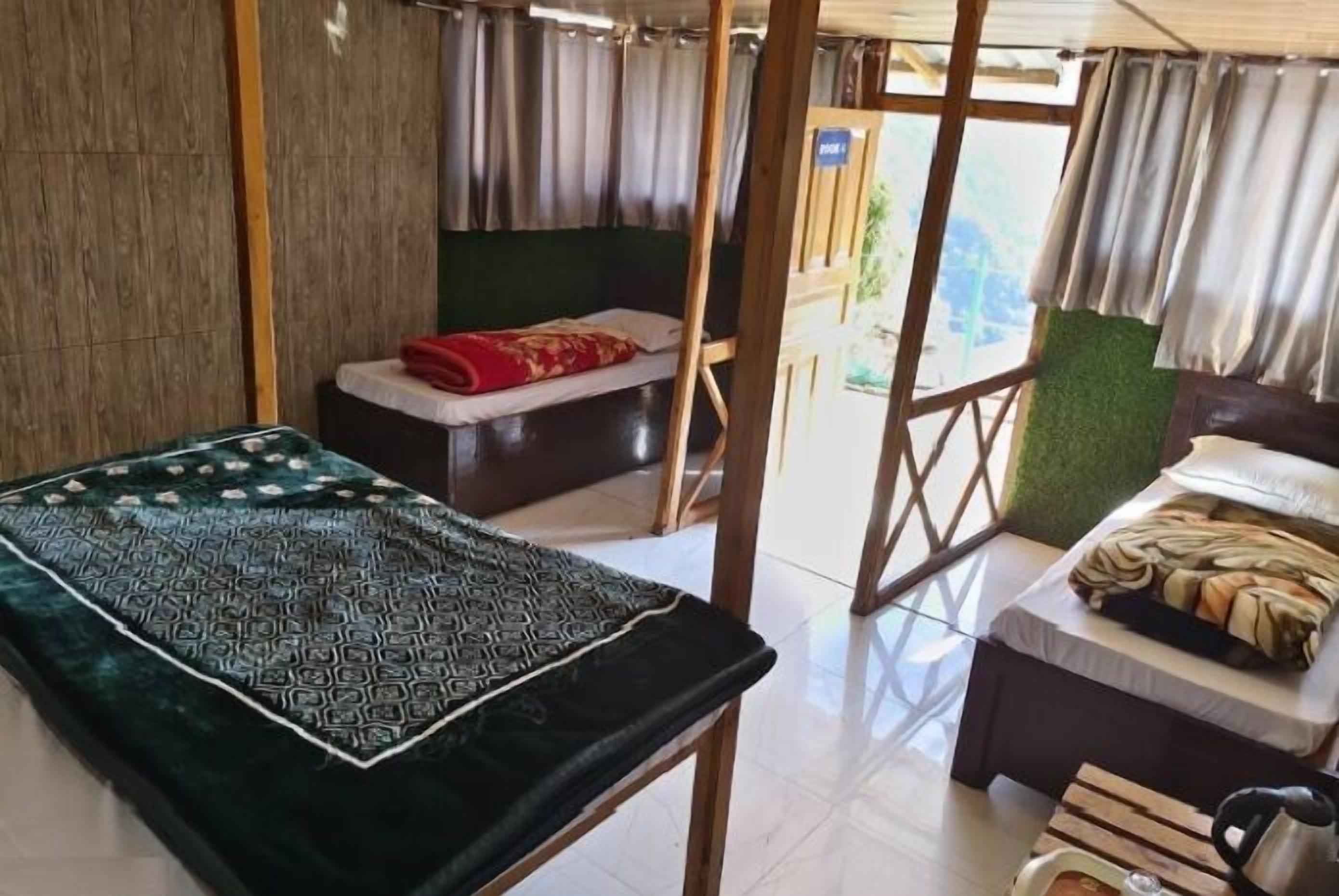 A room with a bed, a small bench, a table with a kettle, and a view through a wooden lattice.