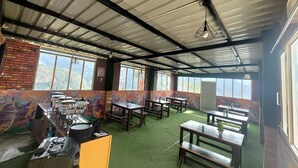 A dining area with tables and chairs, a brick wall, and large windows. - Anany Resort (Pangoot)