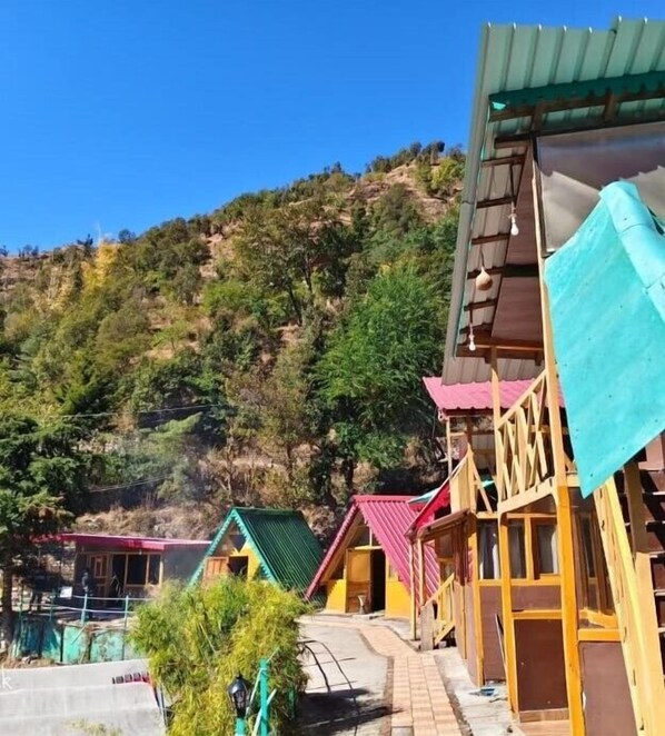 A row of wooden cabins with sloped roofs, set against a hillside backdrop. - Anany Resort (Pangoot)