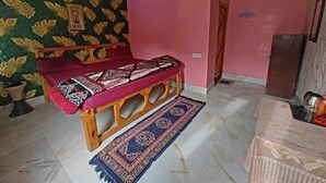A room with a bed, a wooden bench, a patterned rug, and a wall with floral wallpaper. - Anany Resort (Pangoot)