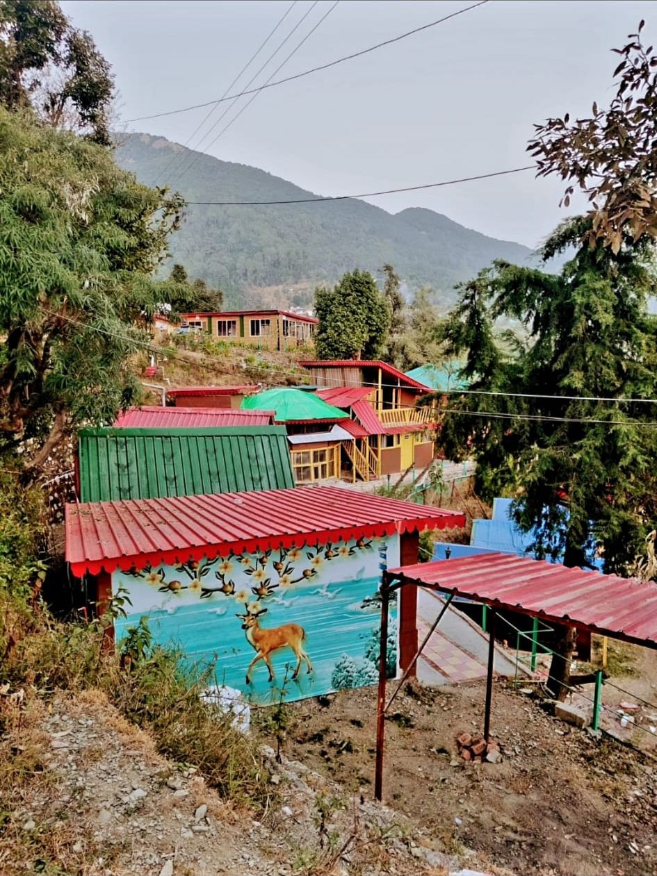 Un pueblo rural con casas coloridas, un mural de un ciervo y montañas al fondo.