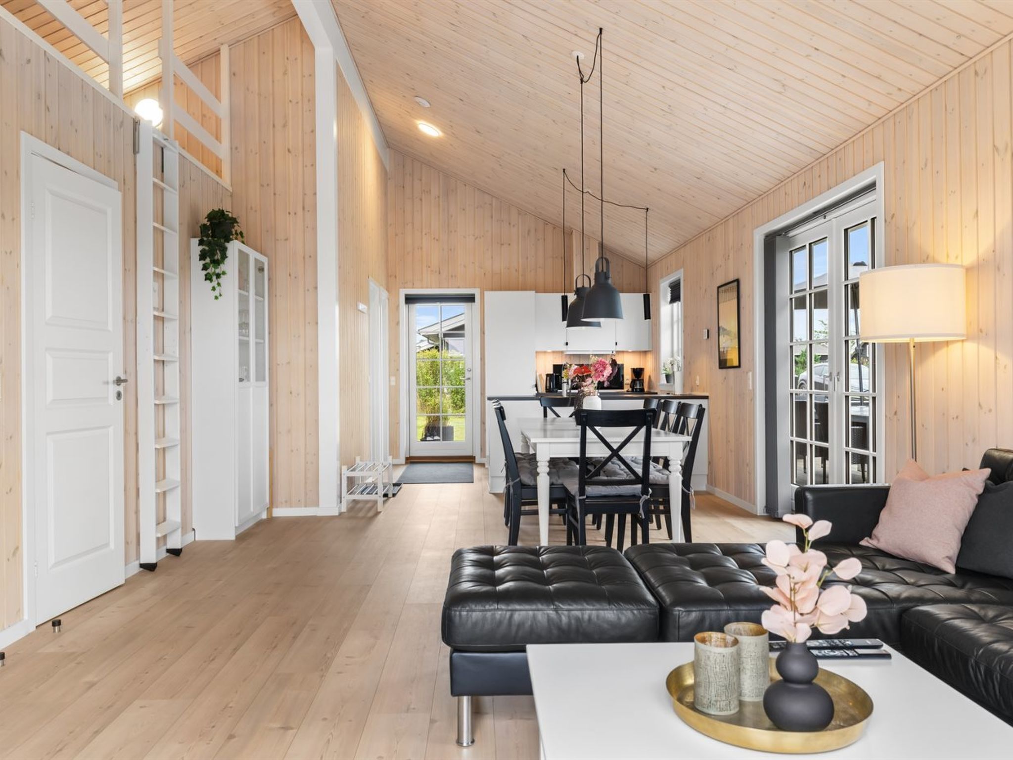 A spacious living area with a black leather sofa, a white coffee table, and a dining area with a black table and chairs.