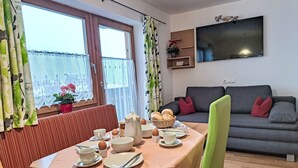 A dining area with a table set for breakfast, a sofa, and a TV in the background. - Fichtenblick by Interhome (Wildschönau)