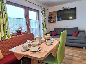 Ein Essbereich mit einem für das Frühstück gedeckten Tisch, einer Couch und einem Fernseher im Hintergrund.