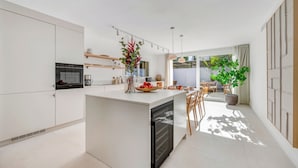 A modern kitchen with white cabinetry, a central island, and a dining area with wooden chairs and a table. - Villa Ava by Vacation Marbella (Estepona)