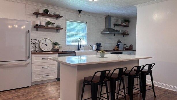 Una cocina moderna con armarios blancos, una isla central con taburetes y un horno empotrado.