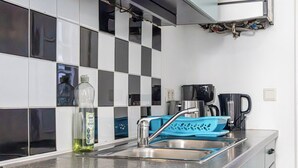 Une cuisine avec un évier en acier inoxydable, un égouttoir bleu et une bouteille de liquide vaisselle.