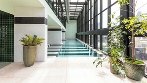 A modern indoor space with a glass staircase, potted plants, and a view of the city. - The Queensbridge Contemporary Nostalgia. Heated pool, Gym, Sauna, Steam, Bar (Melbourne)