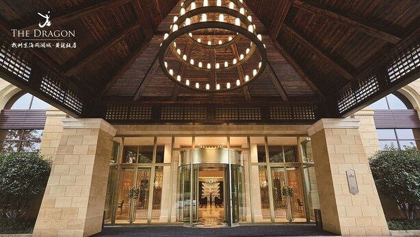A hotel entrance with a circular light fixture above the doors, a glass revolving door, and a stone facade. - Hangzhou Leisure Lake The Dragon (Hangzhou)