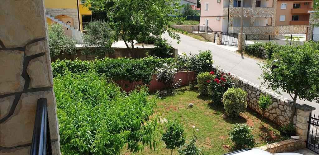 Un barrio residencial con un muro de piedra, un pequeño jardín con diversas plantas y una carretera al fondo.