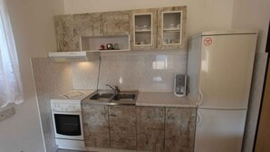 Een kleine keuken met een ingebouwde oven, een dubbele spoelbak en een koelkast.