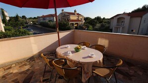 Een ronde tafel met vier stoelen en een rode parasol op een balkon met een stenen vloer.