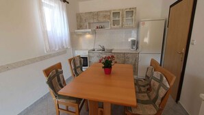 Een kleine keuken met een eettafel, stoelen, een koelkast en een spoelbak.