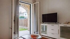 Una habitación con una puerta corrediza de vidrio que da a un patio, un televisor de pantalla plana sobre un mueble, y una pequeña mesa con una caja encima.