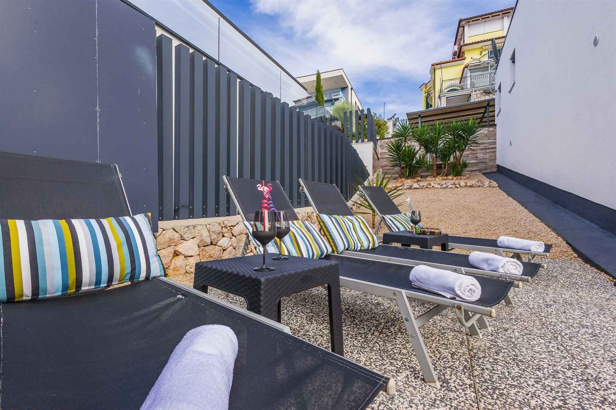 A rooftop terrace with lounge chairs, a table with a wine glass, and a stone wall.