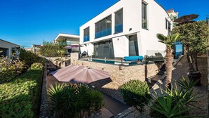 Ein modernes, zweistöckiges Haus mit Swimmingpool, umgeben von viel Grün und blauem Himmel.
