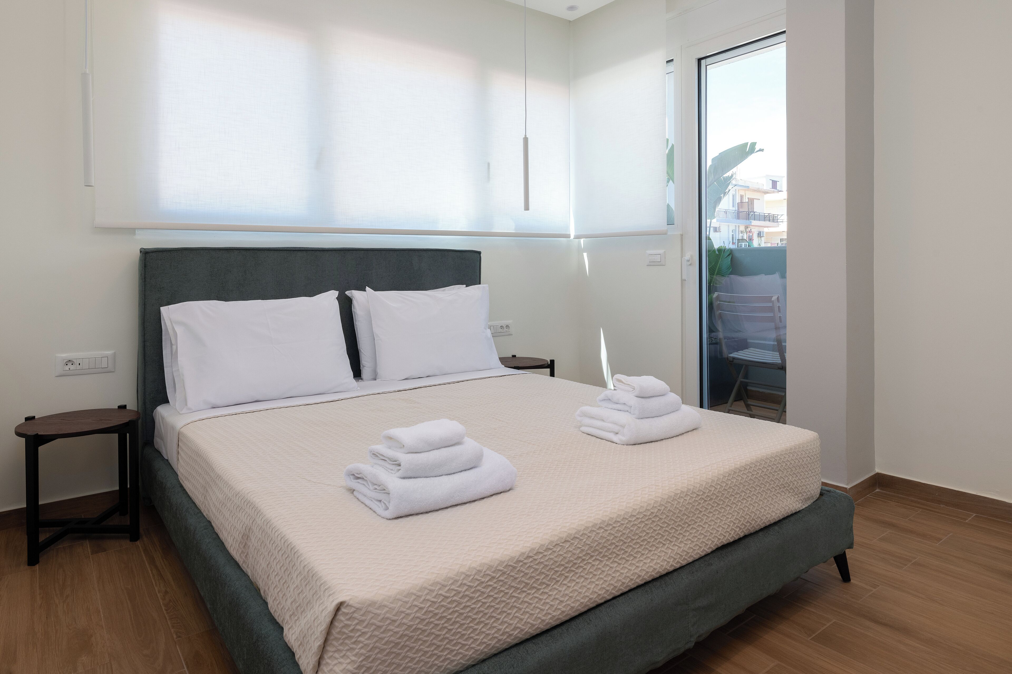 A neatly made bed with white linens and towels, a bedside table, and a view of the outside balcony.