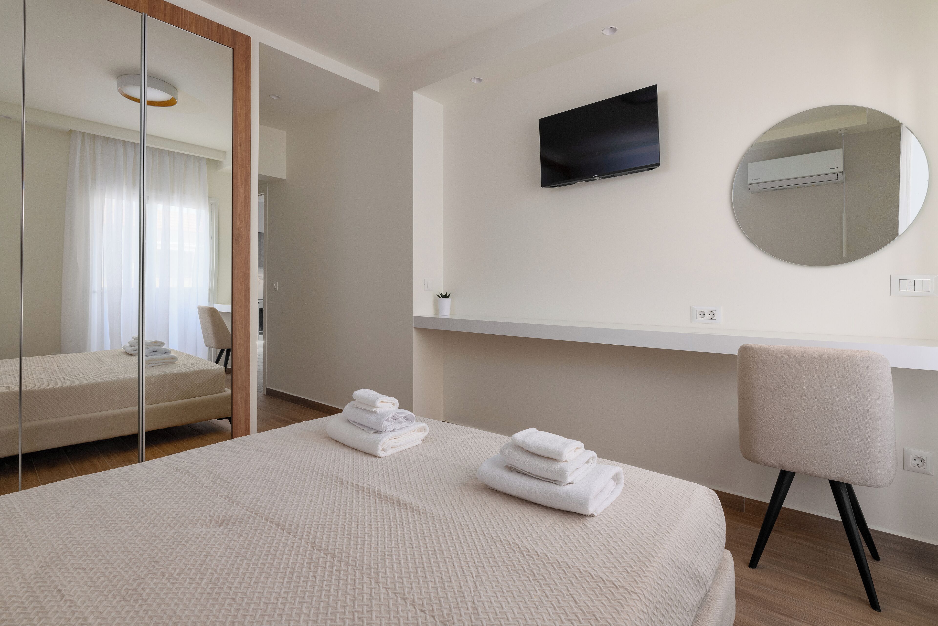 Ein modernes Hotelzimmer mit einem großen Bett, einem an der Wand montierten Fernseher, einem runden Spiegel und einem Schreibtisch mit Stuhl.