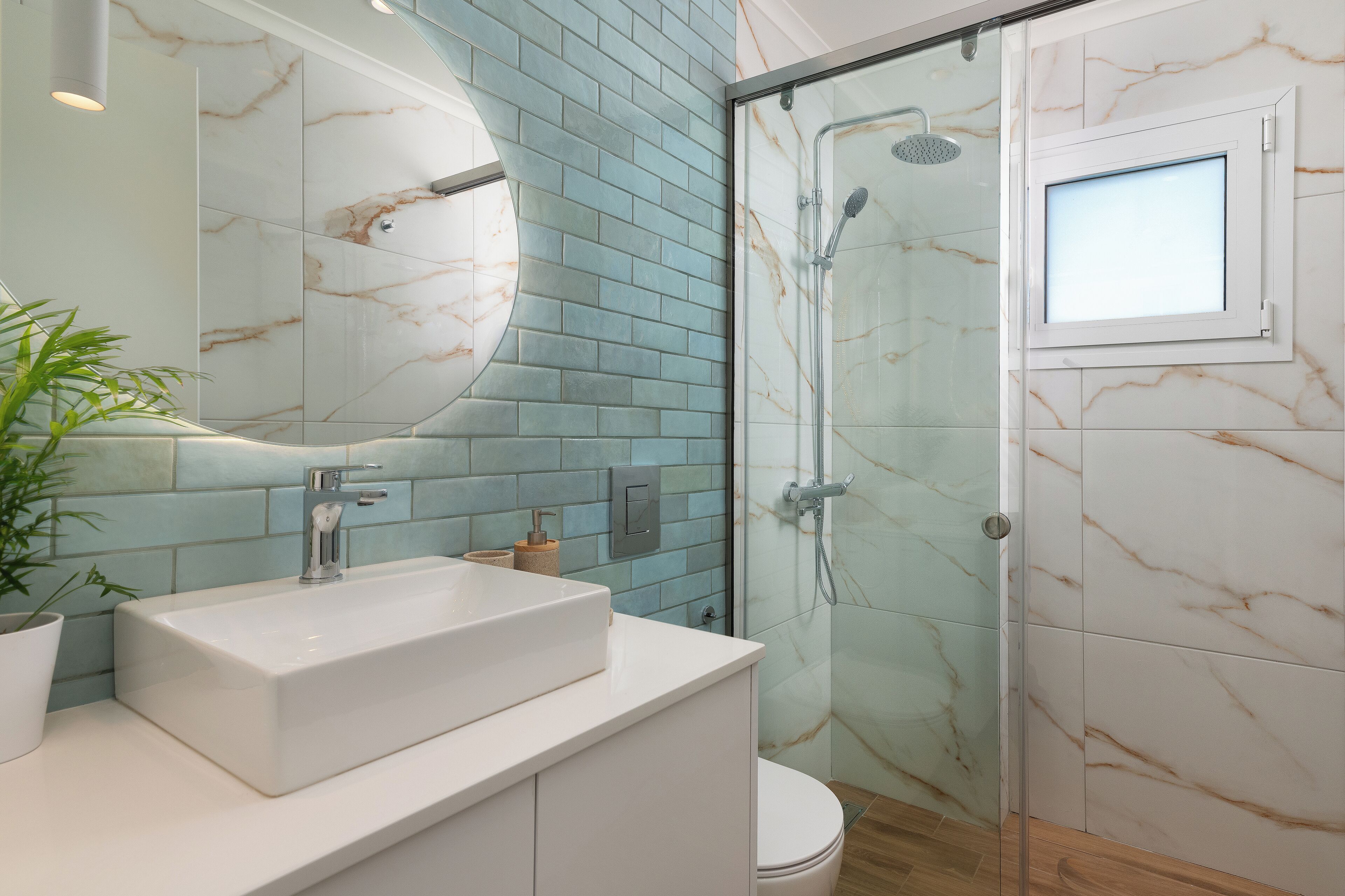 Ein Badezimmer mit weißem Waschbecken, einer Duschkabine aus Glas und einer Wand mit Marmorfliesen.