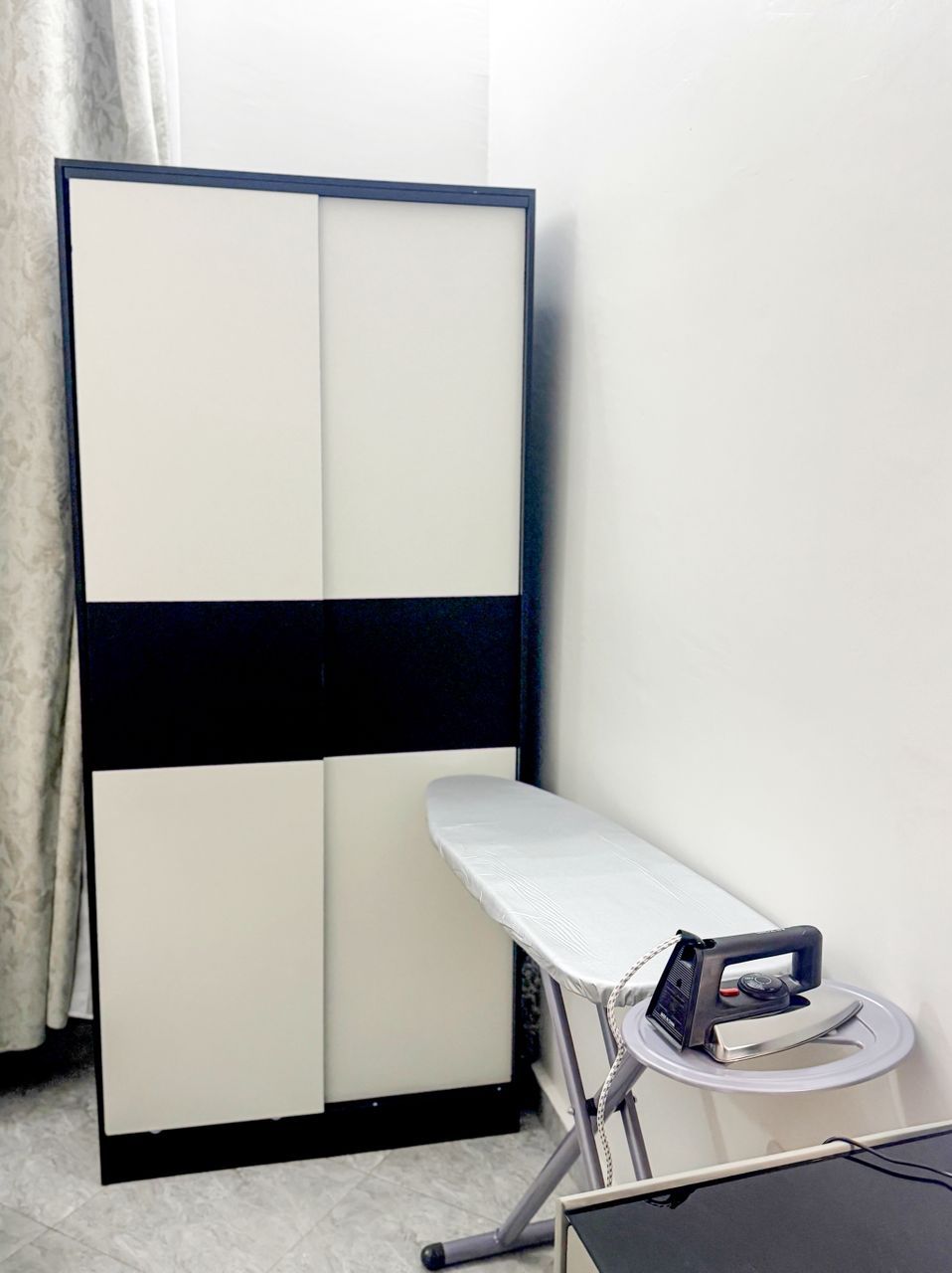 A room with a large, dark-colored cabinet with a white top, a small ironing board with an iron, and a small table with a device on it.