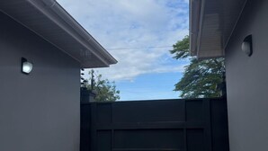 Un espacio al aire libre techado, con piso empedrado, una reja negra y cielo despejado.