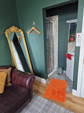 Ein Zimmer mit einem großen Spiegel, einem hölzernen Kleiderbügel, einer Duschkabine, einem weißen Waschbecken und einem roten Handtuch.