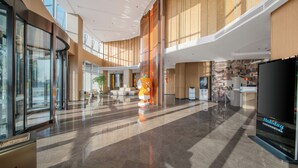 Egy tágas előcsarnok, melyben egy nagyméretű, narancssárga színű embléma található, emellett van egy recepciós pult és egy nagy képernyő, amelyen a „Holiday Inn Express” felirat látható.